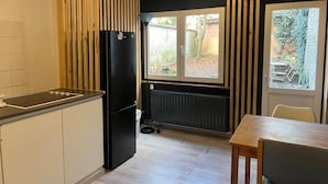 A compact kitchen with a black refrigerator, a wooden cabinet, and a window overlooking a garden. - European District Studios (Brussels)