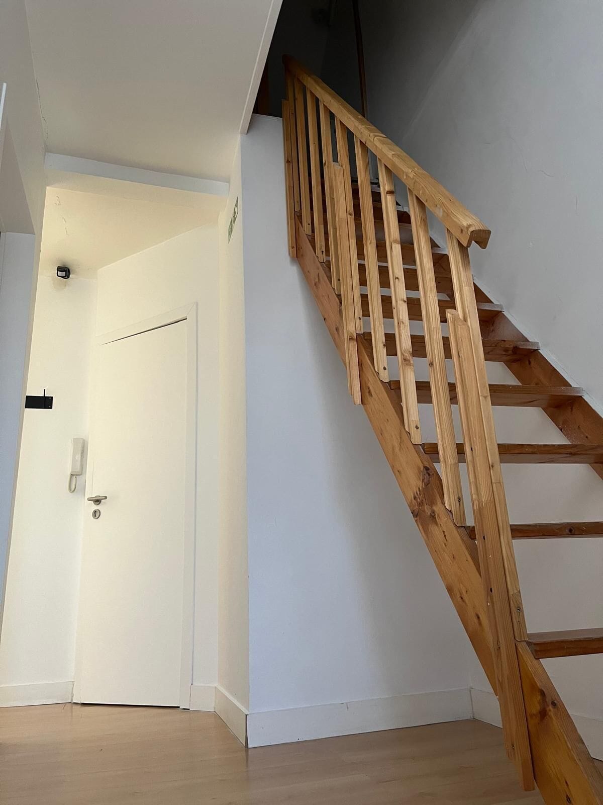A wooden staircase with a handrail leading to a white door.