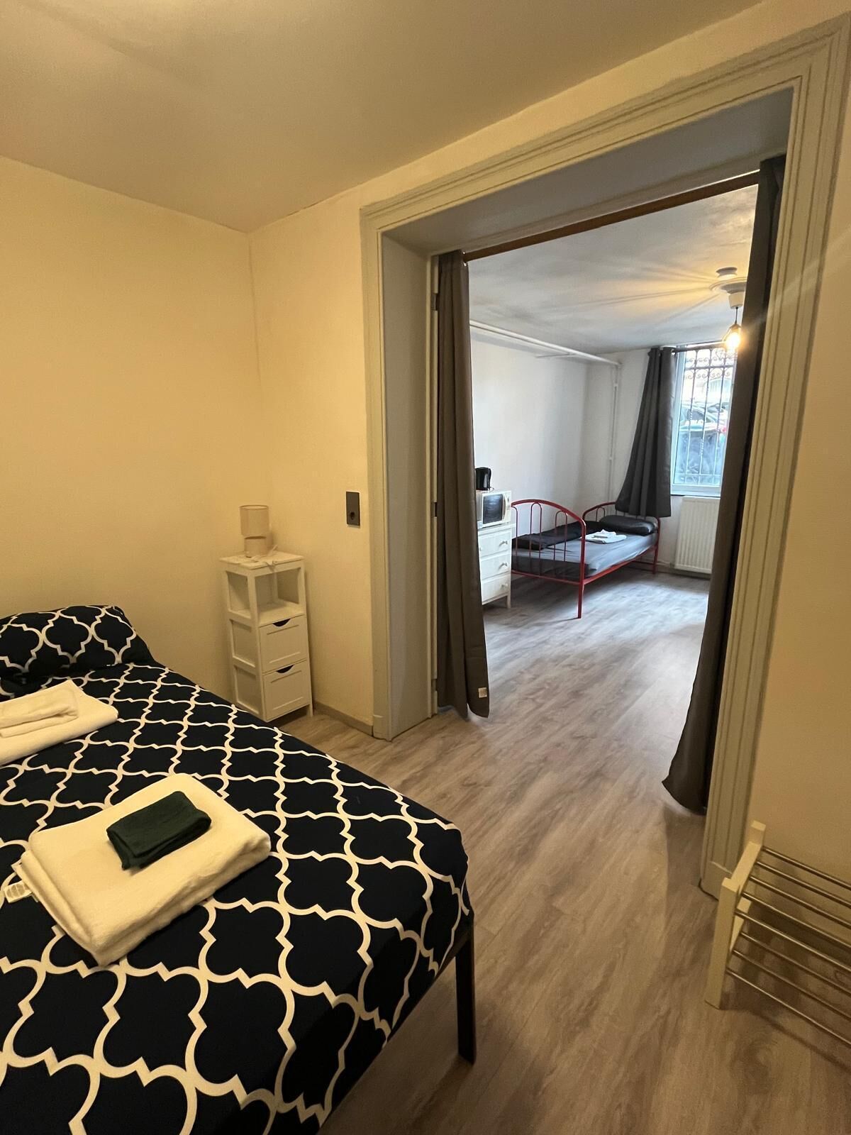 A bedroom with a bed, a bedside table, and a chair. There is a window with curtains and a view of the outside.