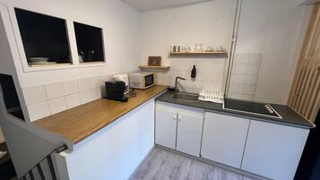 Een kleine keuken met witte kasten, een houten aanrecht, een magnetron, een koffiezetapparaat en een spoelbak.