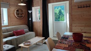 A cozy room with a wooden interior, a sofa, a small table, a dining table with chairs, a window with a view of greenery, and a ceiling fan. - En Pleine Nature Mas Cévenol Calme Sans vis à Vis, Baignade à Proximité (BREAU-MARS)