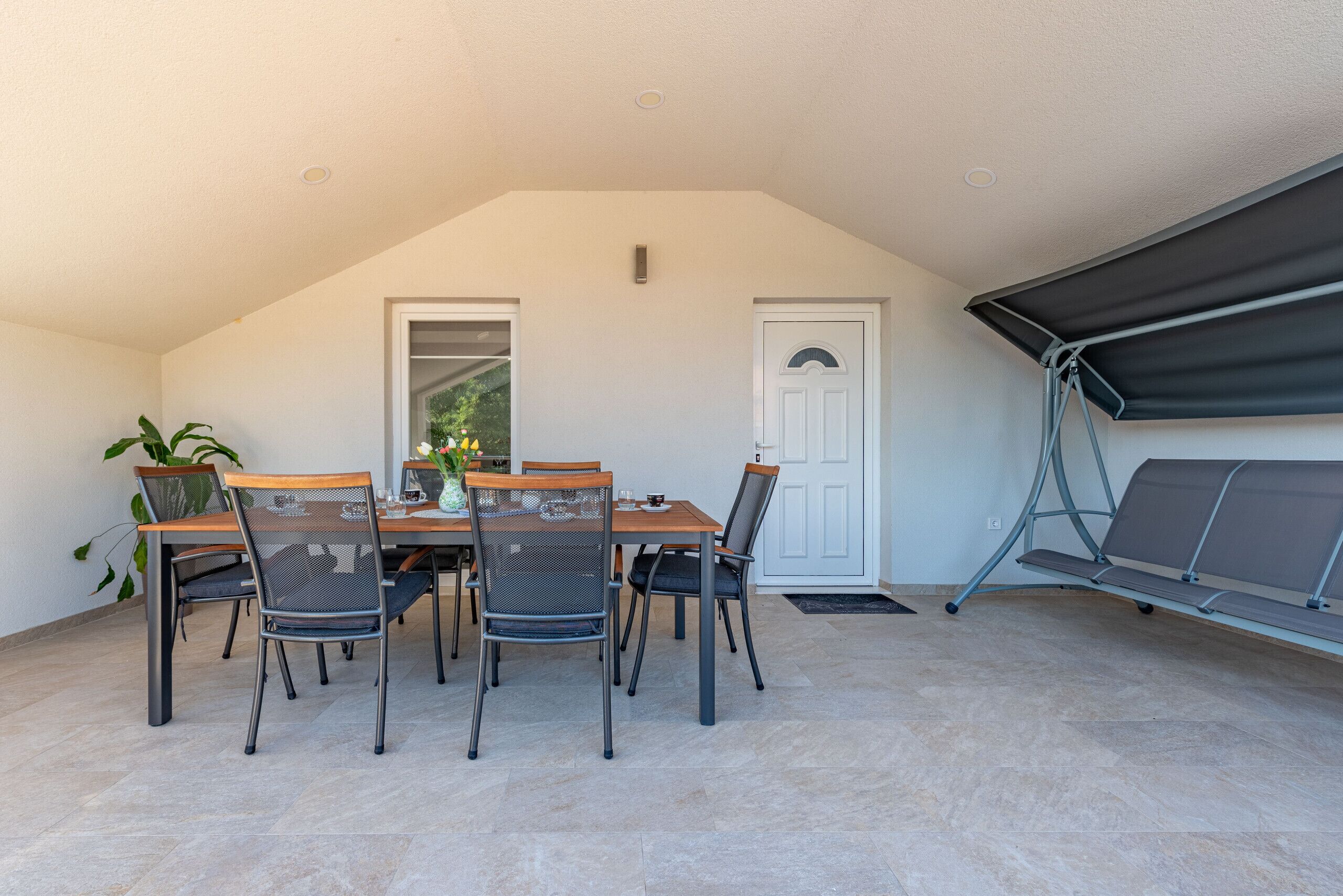 A covered patio with a dining table and chairs, a bench, and a door.