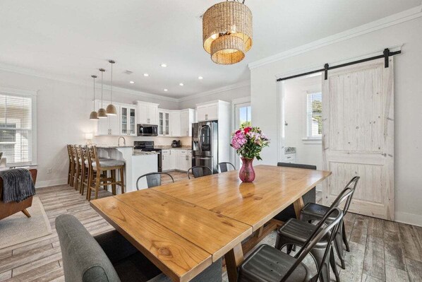 A spacious kitchen with white cabinets, a wooden dining table, and a hanging light fixture.
