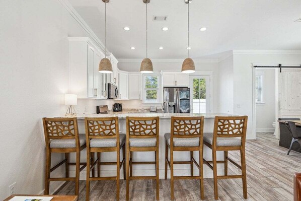 A kitchen with five wooden bar stools, white cabinets, and pendant lighting.