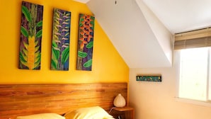 A bedroom with a wooden headboard, a bed with yellow bedding, and three paintings of leaves on the wall. - Gite Deshroses Dans Petite Résidence Avec Piscine (Deshaies)
