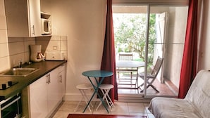 A compact kitchen with a microwave, toaster, and sink. There is a small table with chairs and a sofa in the adjacent living area. - Gite Deshroses Dans Petite Résidence Avec Piscine (Deshaies)