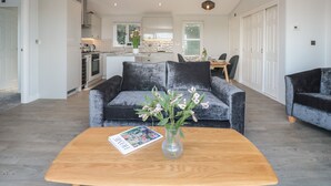 A modern living room with a grey sofa, a wooden coffee table with a magazine, and a vase with flowers. - Bluebell Lodge (Dartmouth)