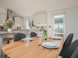 A modern kitchen with white cabinets, a wooden dining table set for four, and a view of the outdoors through a large window.