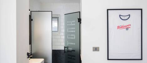 Ein modernes Badezimmer mit Glasabtrennung, einem gerahmten T-Shirt an der Wand und einem gefliesten Duschbereich.