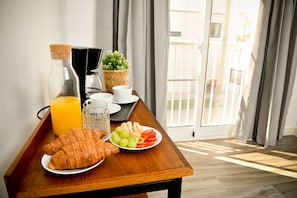 A breakfast table with croissants, fruit, and juice, near a window with curtains. - Honky Tonk Punta Cana (Punta Cana)