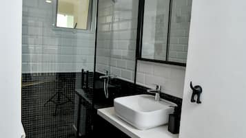 Casa de banho moderna com lavatório branco, bancada preta e cabine de duche em vidro.