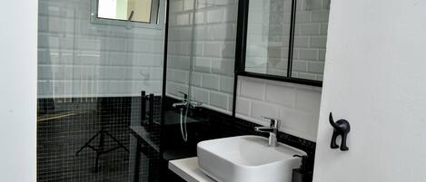 A modern bathroom with a white sink, black countertop, and a glass shower enclosure.