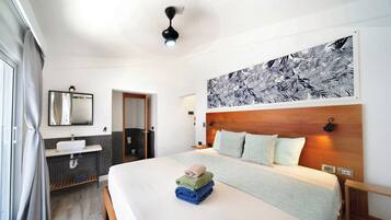 A hotel room with a bed, a large wall art piece, a bathroom with a sink and mirror, and a view of the outside.