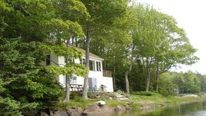 Un chalet au bord du lac, doté d’un quai, et entouré d’une forêt dense.