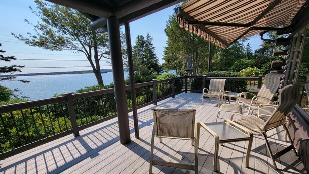 A covered deck with wooden flooring, metal railings, and wicker furniture. - Salt Water Lodge: Spacious 4-bedroom getaway in scenic Boothbay Harbor, ME. (Boothbay Harbor)