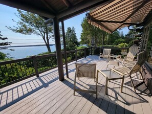 A covered deck with wooden flooring, metal railings, and wicker furniture. - Salt Water Lodge: Spacious 4-bedroom getaway in scenic Boothbay Harbor, ME. (Boothbay Harbor)