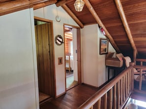 Un escalier en bois mène à une chambre à coucher située dans une mezzanine, offrant une vue sur l’extérieur.