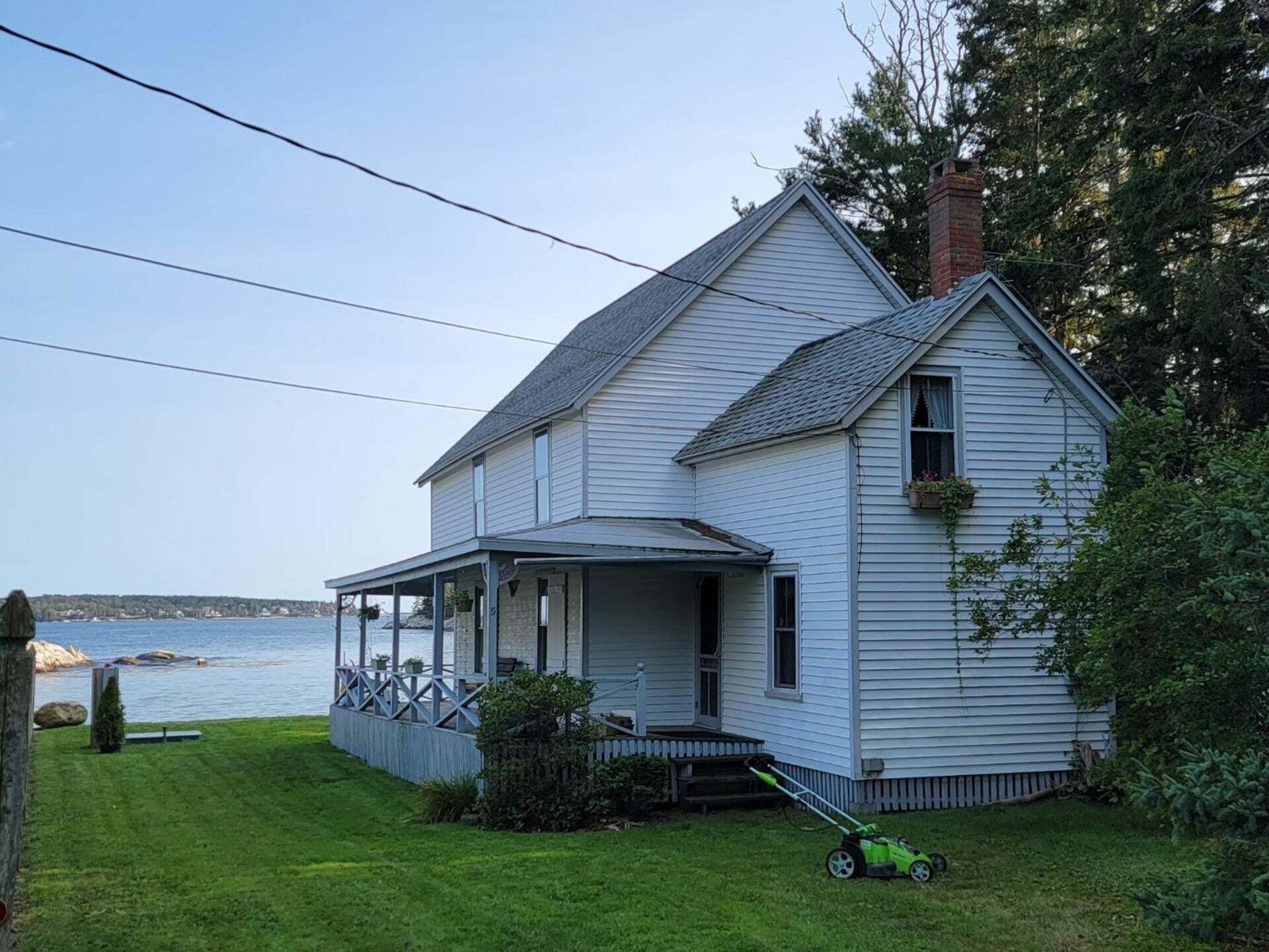 A two-story house with a porch, a lawn, and a view of the water.