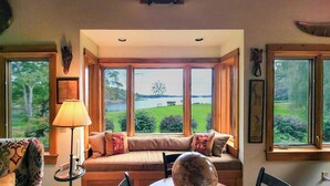 A cozy seating area with a view of a lake and greenery. - Experience coastal charm at Tidewatch in Boothbay, a spacious 3-bedroom home near the ocean. (Boothbay)