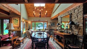 A cozy dining area with a stone fireplace, wooden beams, and a chandelier. - Experience coastal charm at Tidewatch in Boothbay, a spacious 3-bedroom home near the ocean. (Boothbay)
