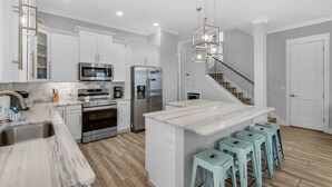 A modern kitchen with white cabinets, stainless steel appliances, a marble island, and light blue bar stools. - 🌴 Sea Ya Sun 4BR | FAB Kitchen • 2 Pools • Miramar Beach 🏖️ (Miramar Beach)