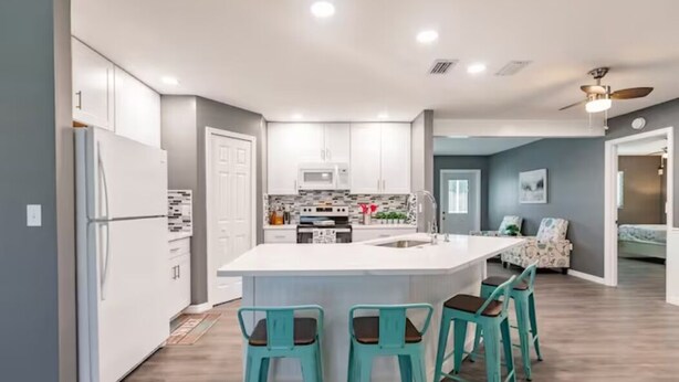Een moderne keuken met een centraal eiland, witte kasten en teal barstoelen.