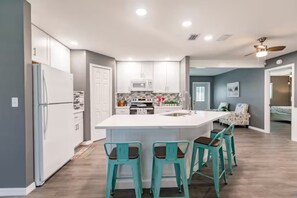 Une cuisine moderne dotée d’un îlot central, de meubles blancs et de tabourets de bar de couleur turquoise.