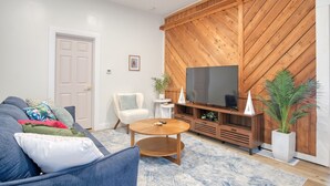 Ett vardagsrum med en blå soffa, en TV-möbel i trä, en platt-TV och en krukväxt.