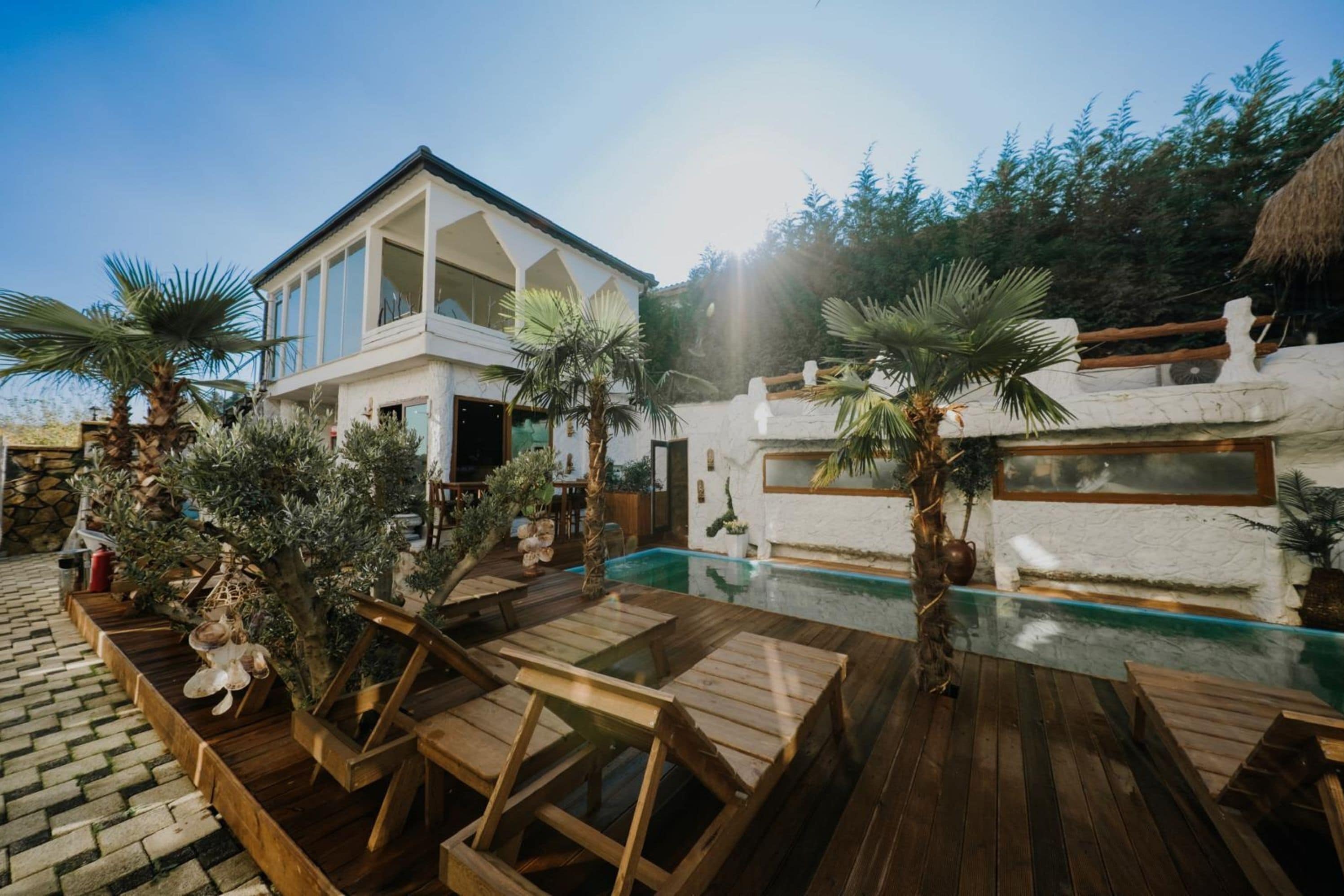 A modern house with a pool, wooden deck, and palm trees.