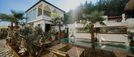 A modern house with a pool, wooden deck, and palm trees.