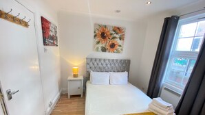 Quarto bem arrumado com uma cama, luminária, cabideiro e uma janela com cortinas.