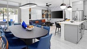 Cocina moderna con isla central, comedor con sillas azules y un ventanal con vistas a un balcón.