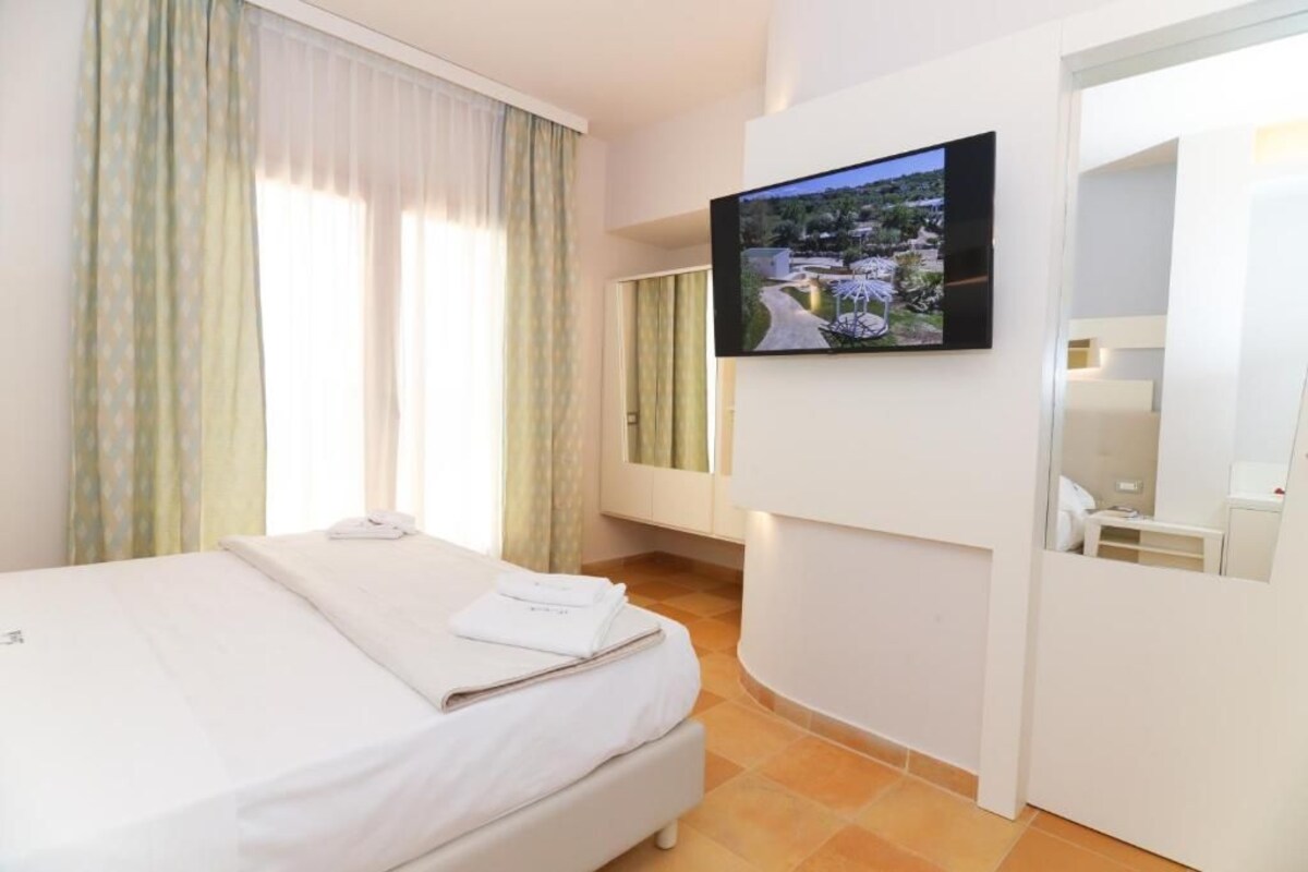 Habitació d'hotel amb un llit, una televisió penjada a la paret i una finestra amb cortines.