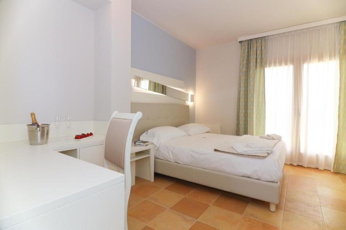 A hotel room with a bed, a desk with a chair, a minibar, and a window with curtains.