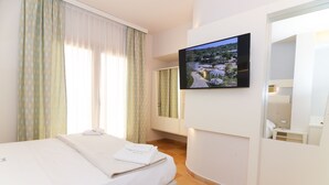 A hotel room with a bed, a TV mounted on the wall, and a window with curtains. - Resort Agave Blu (Ricadi)