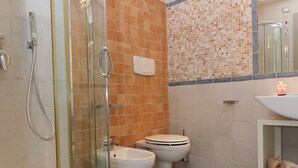 A bathroom with a glass-enclosed shower, two toilets, a sink, and a tiled floor. - Resort Agave Blu (Ricadi)