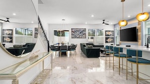 A modern living room with a marble floor, a dining area with a glass railing, a sofa, and a bar area with stools.