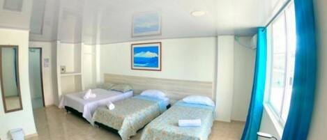 A hotel room with two single beds, a large window with blue curtains, and a painting of a beach on the wall.