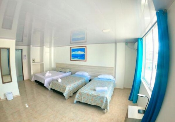 A hotel room with two single beds, a large window with blue curtains, and a painting of a beach on the wall.