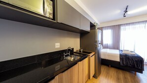 A compact kitchen with a black countertop, stainless steel appliances, and wooden cabinets. - B.Homy - Be Urban Brooklin (São Paulo)