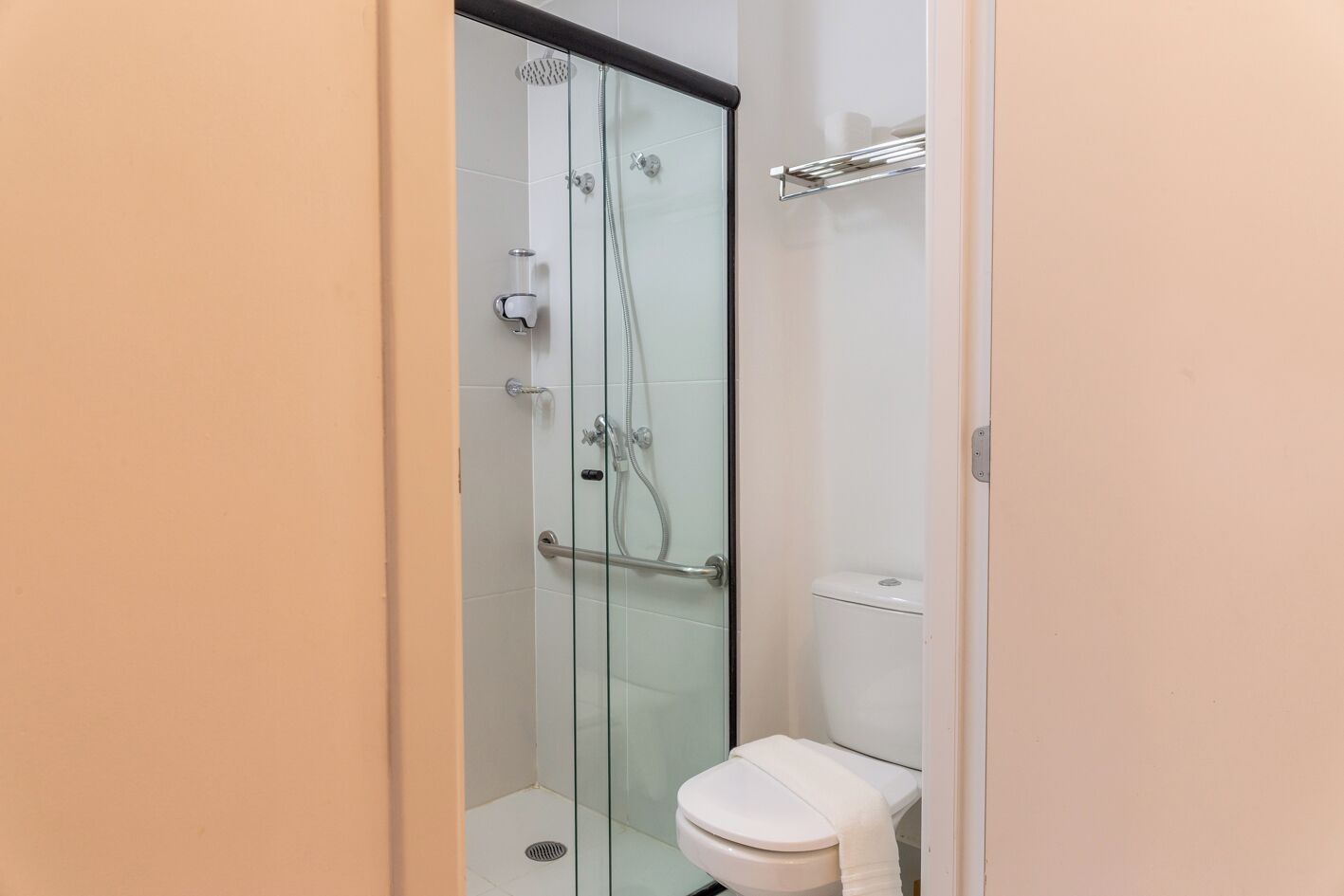 Un baño moderno con ducha acristalada, inodoro blanco y un perchero para toallas.