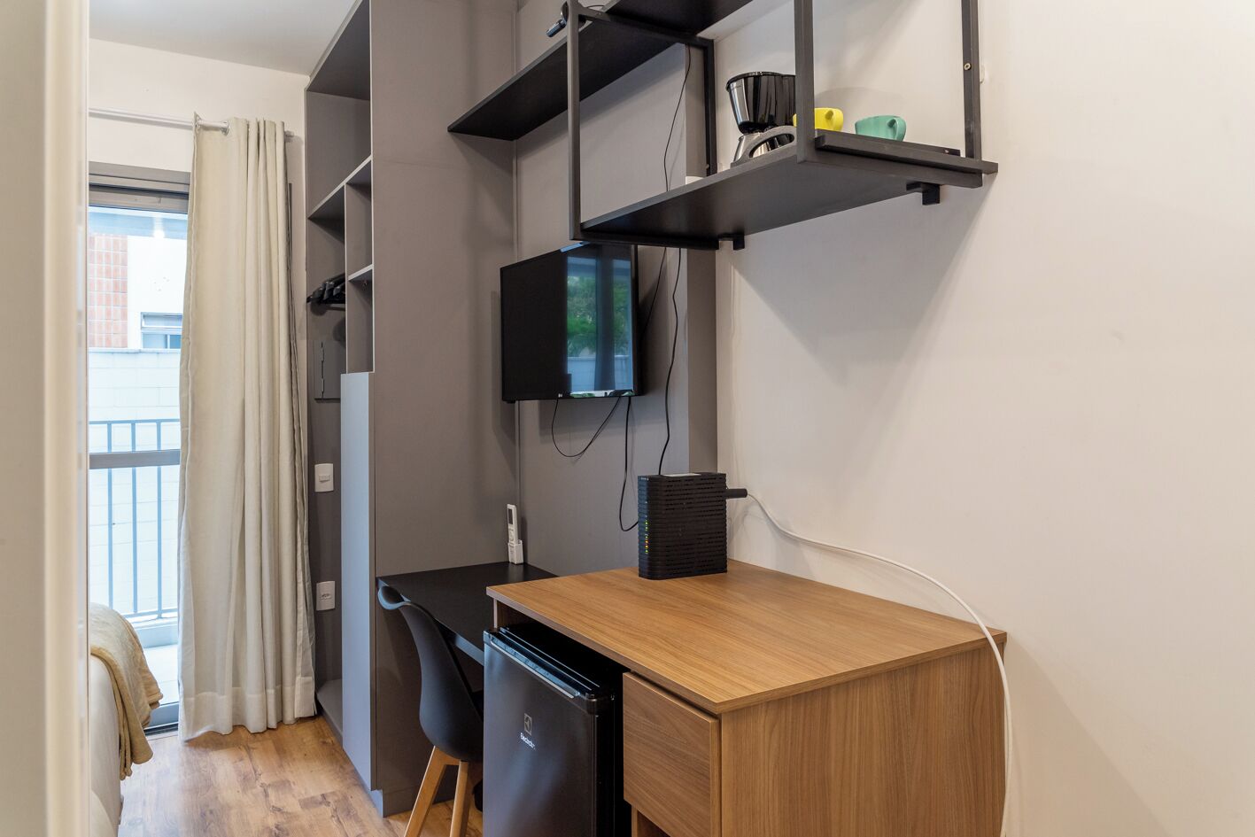 Eine kleine Küche mit einer Holzarbeitsplatte, einem schwarzen Kühlschrank und einem an der Wand befestigten Fernseher.