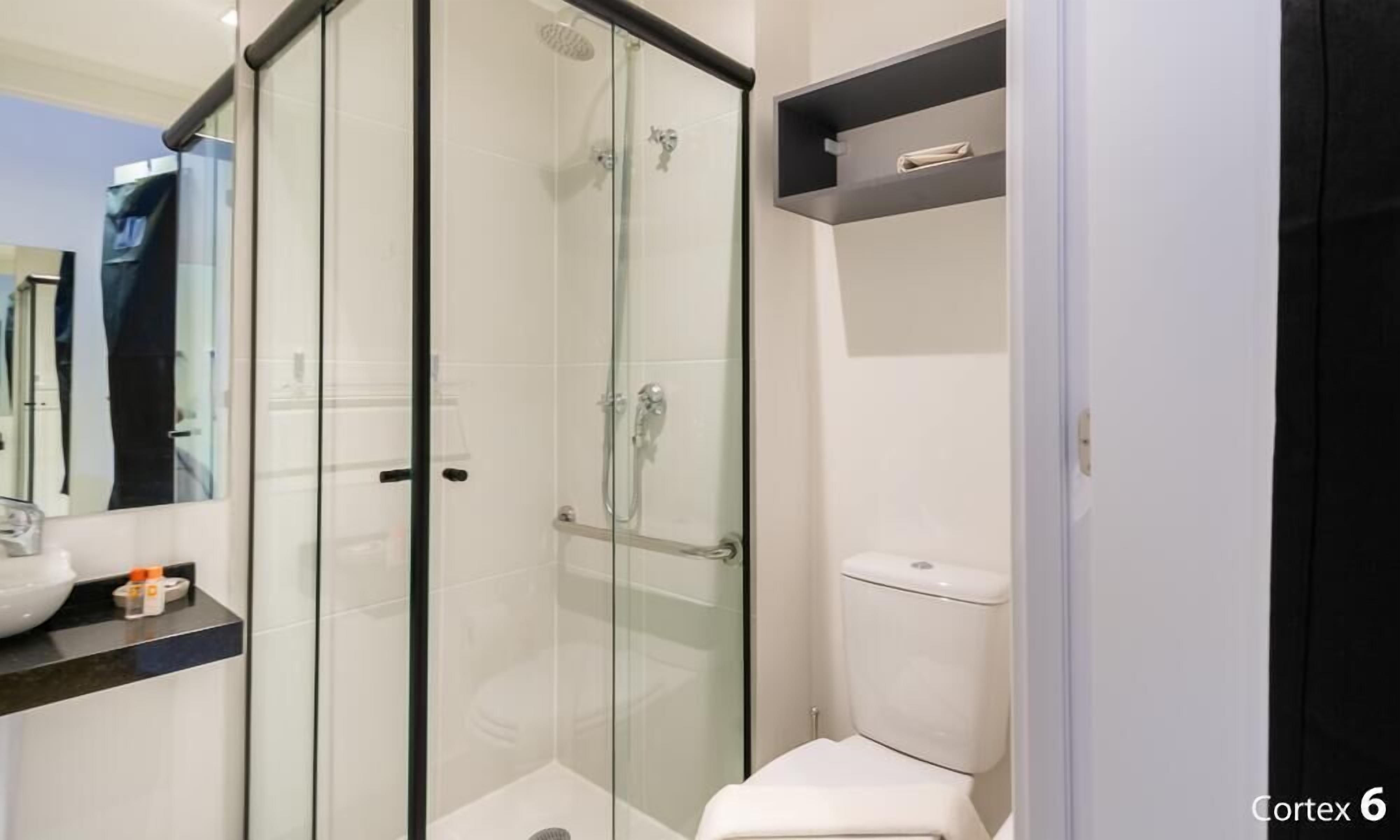 Un baño moderno con ducha envuelta en vidrio, un inodoro blanco y un lavamanos con espejo.