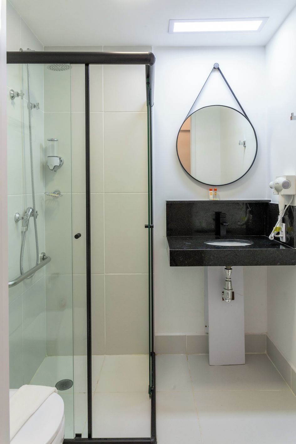 Une salle de bain moderne avec une douche à parois de verre, un lavabo sur un plan de travail noir et un miroir rond.