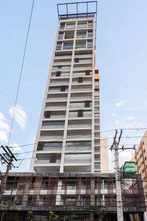 Um edifício alto, com vários andares, apresenta um design arquitetônico moderno, com varandas e uma série de janelas em cada pavimento.