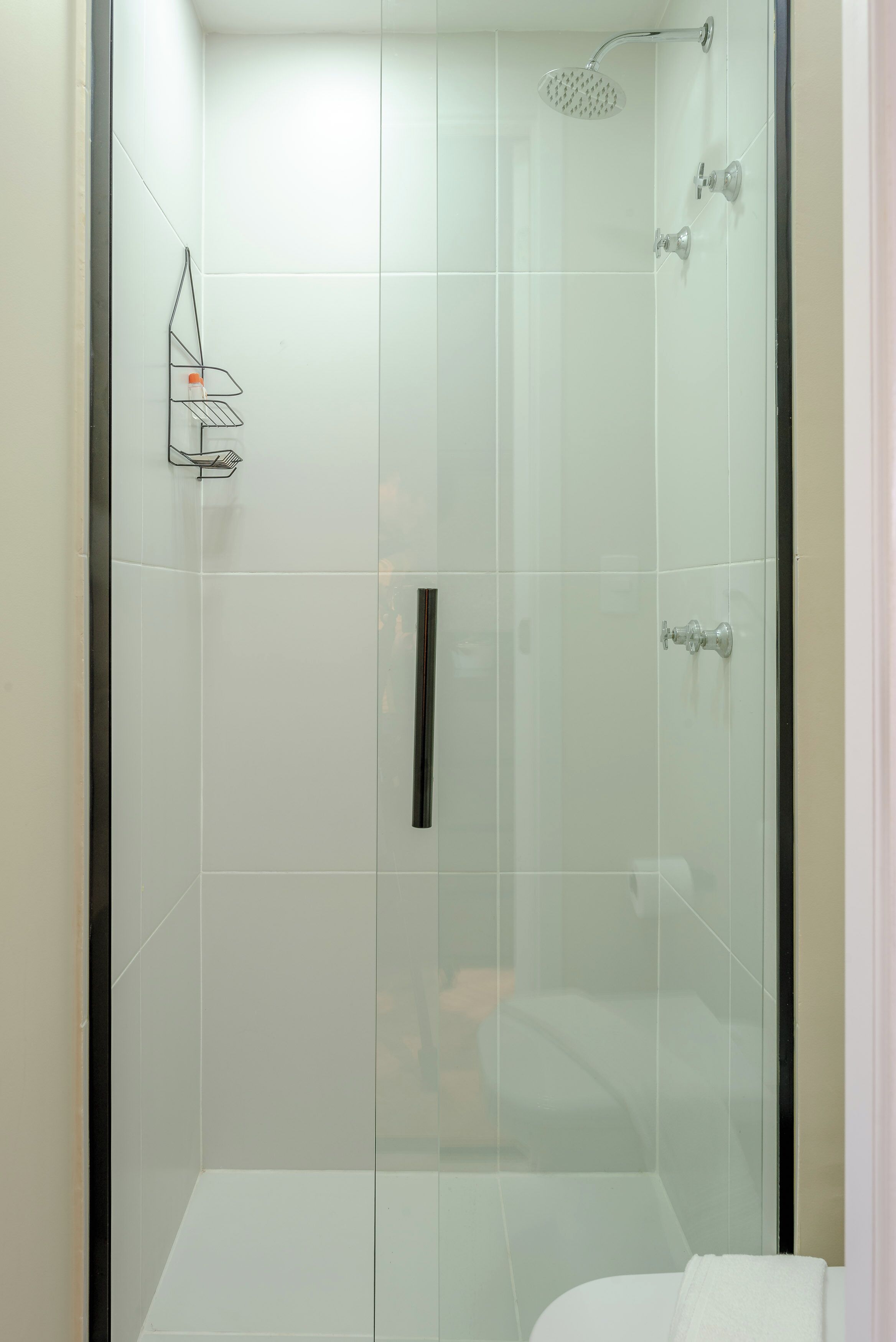 A modern shower with a glass door, a handheld showerhead, and a towel rack.