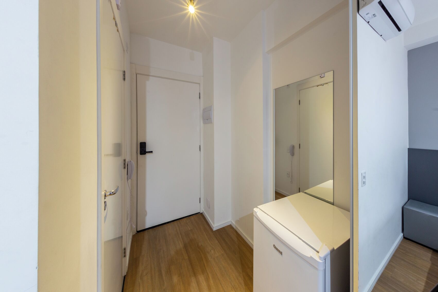 A narrow hallway with a door, a small white appliance, and a mirror on the wall.