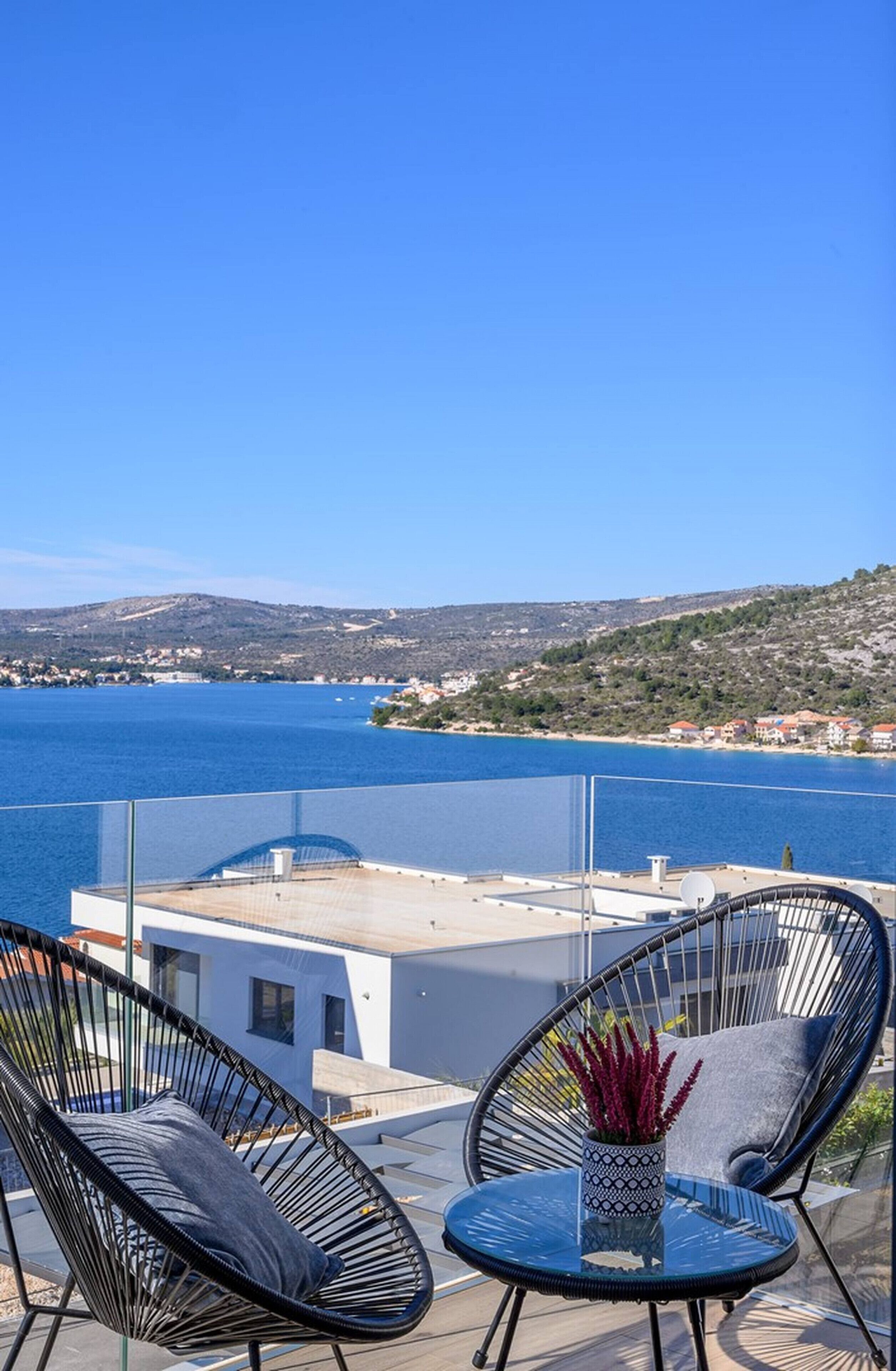 Un balcon avec deux chaises et une table, donnant sur une étendue d’eau et un paysage vallonné.