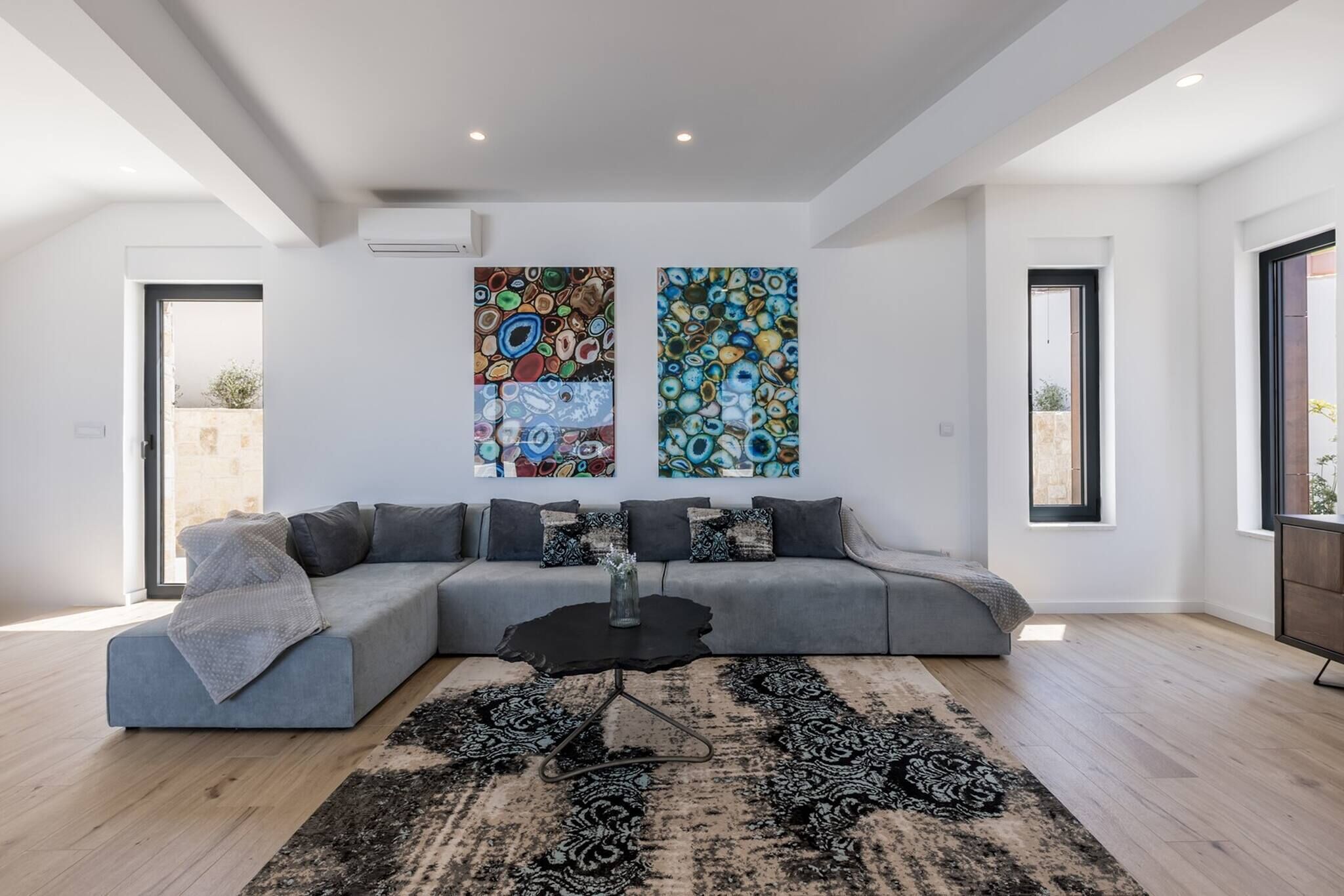 A modern living room with a grey sectional sofa, a black coffee table, and two abstract paintings on the wall.