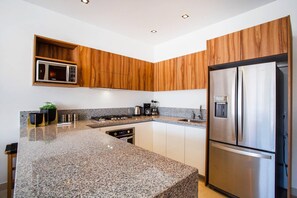A modern kitchen with granite countertops, stainless steel appliances, and wooden cabinetry. - Versalles Retreat | Modern 2-BR w/ Gym & BBQ (Puerto Vallarta)